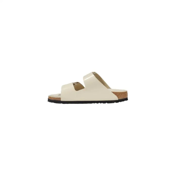Cream-colored two-strap sandal with gold buckles displayed in a product image