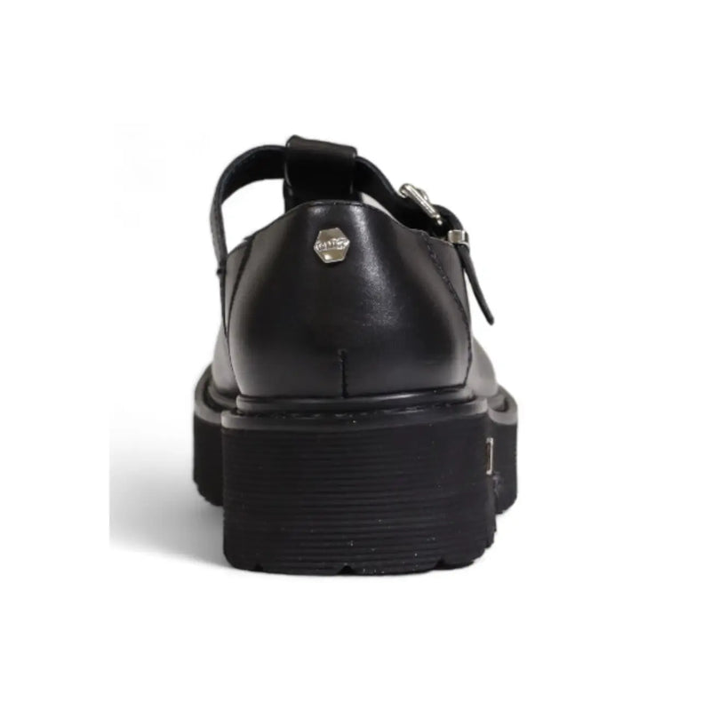 Back view of black leather Cult Women platform sandal with t-strap and silver hexagonal logo plaque on heel