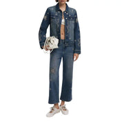 Woman in denim jacket and jeans with embroidery, white bralette, lace-up flats, and white handbag