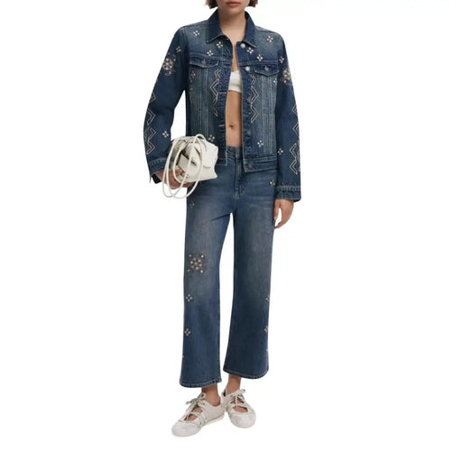 Woman in denim jacket and jeans with embroidery, white bralette, lace-up flats, and white handbag