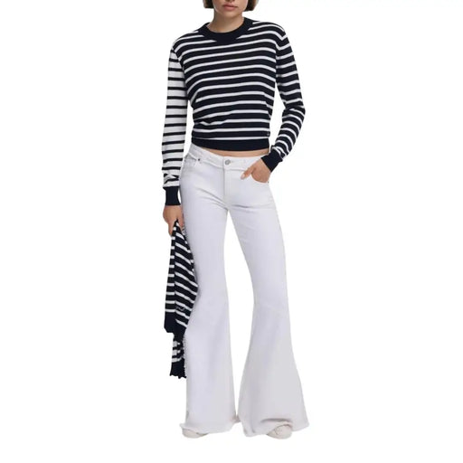 A woman wearing a Desigual women black striped round neck knit sweater in navy and white with white wide-leg jeans