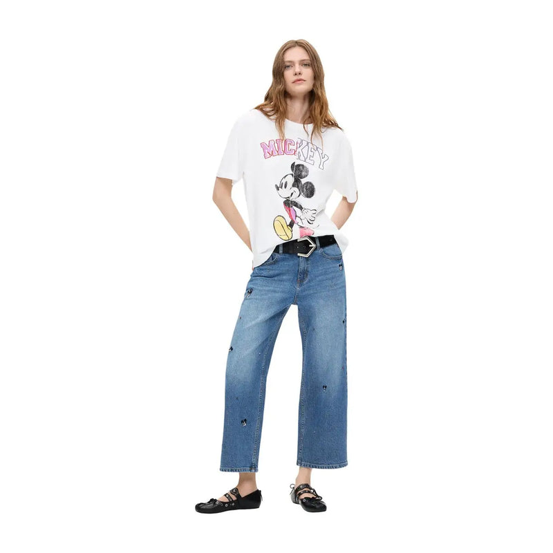 T-shirt blanc à motif Mickey Mouse avec inscription rose et illustration noire et jaune, porté avec un jean en coton bleu Desigual pour femme