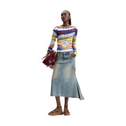 Une femme porte un pull Desigual pour femme en maille viscose bleue à rayures horizontales vives sur les manches longues.