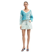 A woman wearing a turquoise and cream patterned knit sweater with long sleeves paired with a light blue Desigual cotton denim skirt