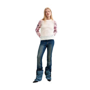Une femme portant un pull Desigual en maille fleurie blanche à manches roses et un jean évasé bleu foncé.