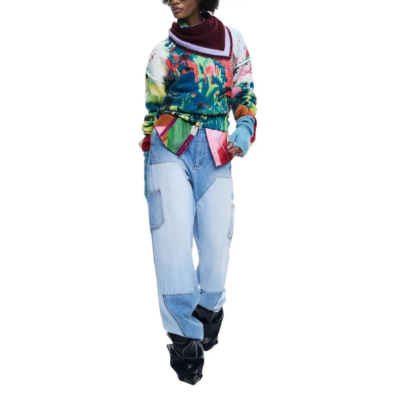Pull long Desigual pour femme, en maille verte acrylique, imprimé abstrait coloré et bordures bordeaux et blanches, porté sur un pantalon en denim patchwork.