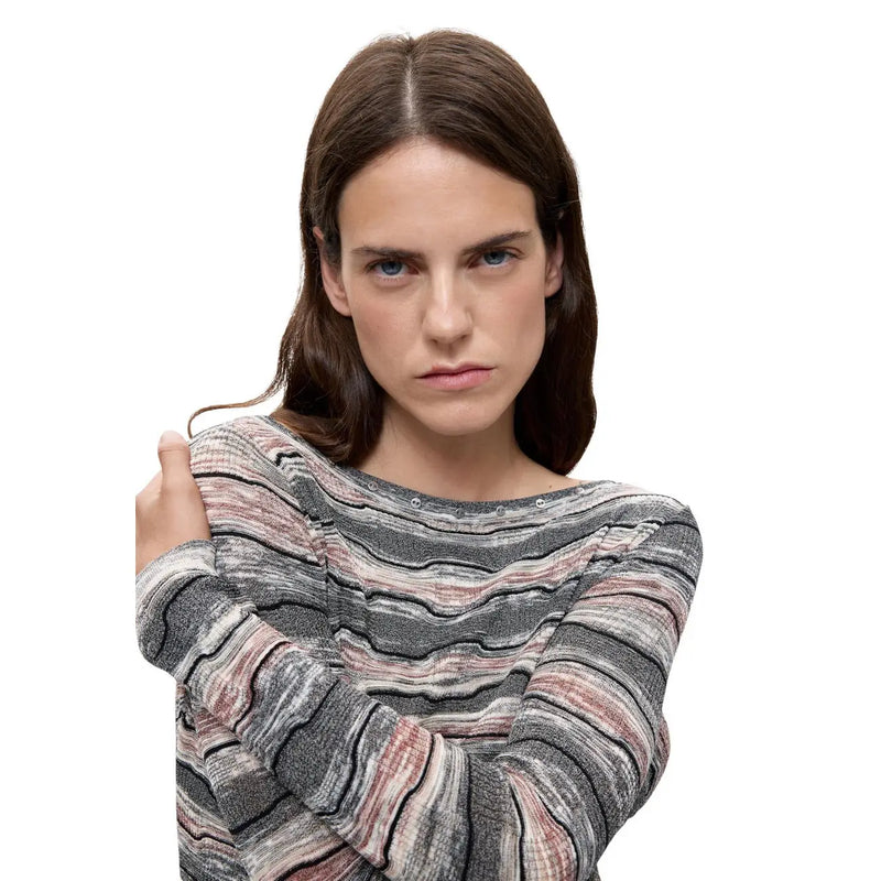 Une femme porte un pull Desigual en maille de coton gris à col bateau et rayures ondulées.