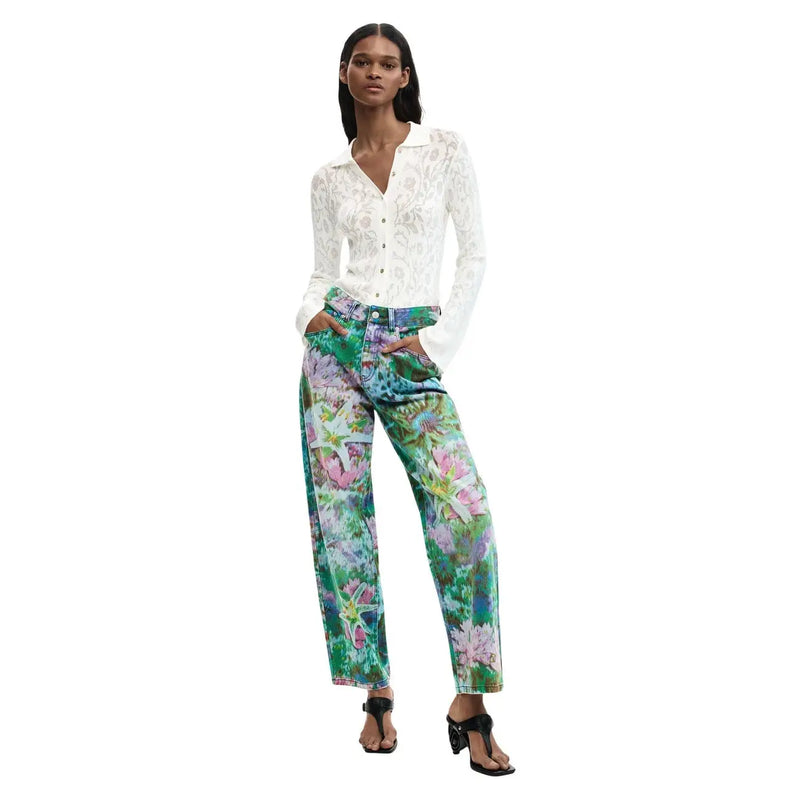 Femme portant un jean Desigual bleu clair en coton à imprimé floral vif et à jambes larges, et une chemise en dentelle blanche.