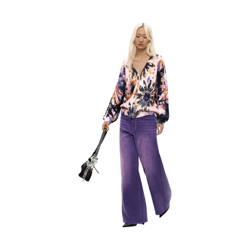 Une femme portant un pull Desigual rose à fleurs en maille de coton, associé à un pantalon violet à jambes larges.