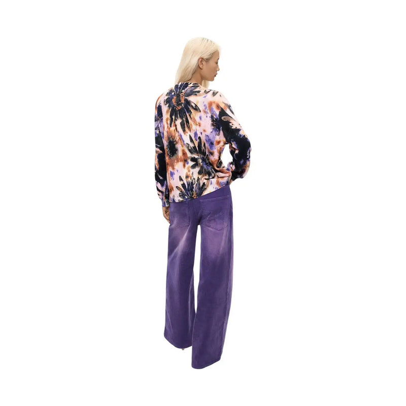 Une femme porte un pull Desigual rose à fleurs en maille de coton avec un chemisier tie-dye violet vif, noir et pêche.