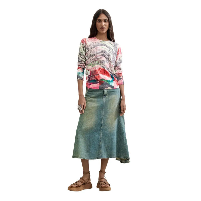 Une femme porte un pull Desigual rouge en maille viscose mélangée à motifs tourbillonnants colorés et une jupe en jean.