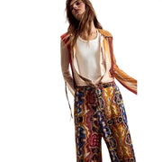 Femme portant un pantalon Desigual pour femme en viscose moutarde avec ceinture, orné d'un motif coloré à jambes larges, et une veste en satin