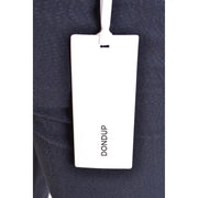 White rectangular dondup brand tag attached to dark navy cotton fabric of men’s spring summer blue trousers