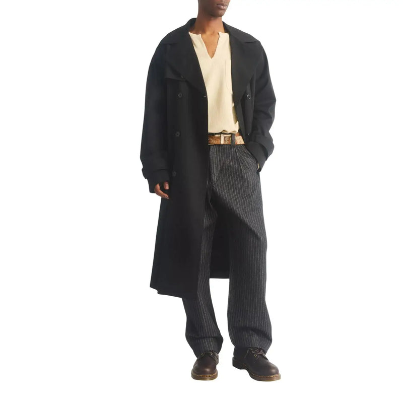Trench-coat noir croisé à col classique et poignets boutonnés, porté avec des bottines Dr. Martens Ambassador en cuir marron pour homme.