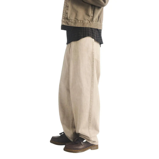 Pantalon en denim beige à jambes larges, coupe décontractée et coutures apparentes, porté avec des mocassins Dr. Martens pour homme en cuir marron, modèle Adrian