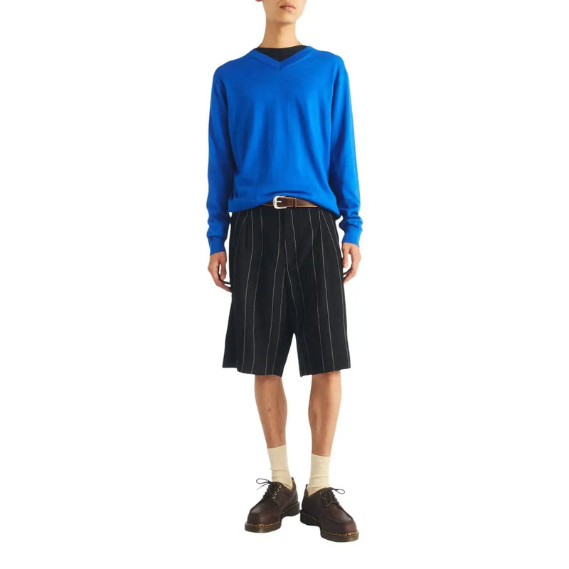 Pull bleu vif à manches longues et col en V porté sur un t-shirt noir, avec des bottines Dr. Martens Lowell marron en cuir pour homme.