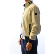 Blouson aviateur couleur crème avec détails de fermeture éclair noirs et écusson rond sur la manche, porté avec un blazer gris en polyester.
