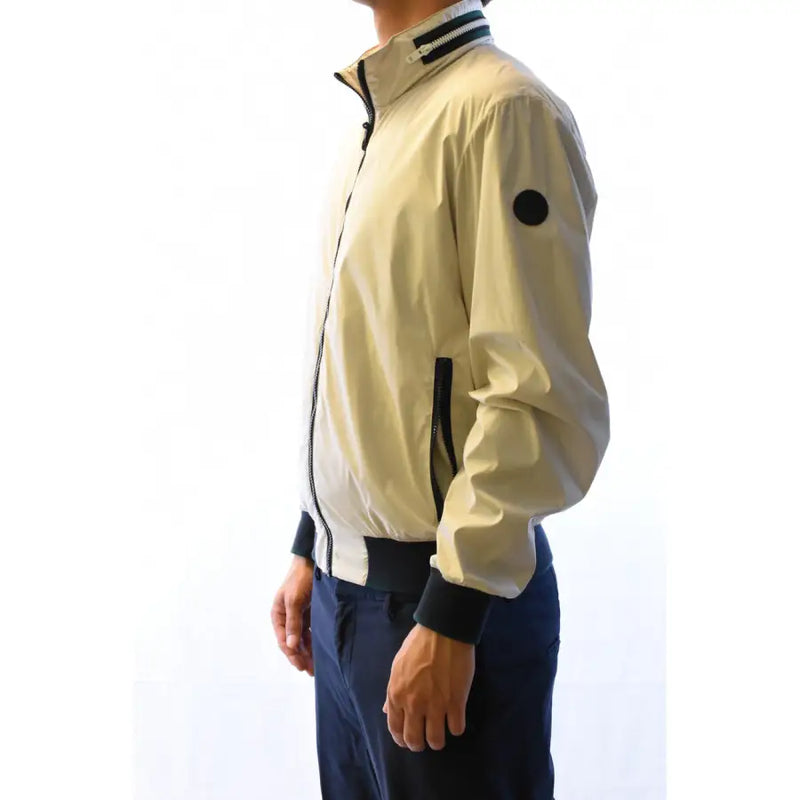Blouson aviateur couleur crème avec détails de fermeture éclair noirs et écusson rond sur la manche, porté avec un blazer gris en polyester.