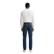 Jean en denim bleu foncé à cinq poches classiques et délavage subtil, porté avec une chemise homme Gant
