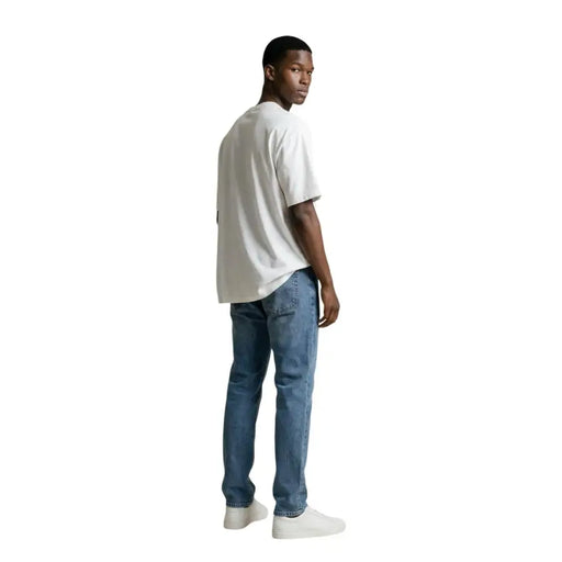 Un homme portant un gianni lupo T-shirt blanc à col rond 100% coton, porté avec un jean bleu délavé.