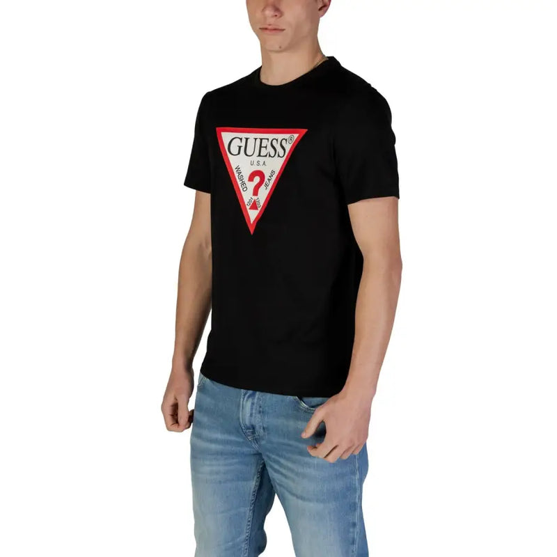Noir Guess hommes t-shirt orné d'un logo triangulaire rouge et blanc audacieux sur lequel le nom de la marque est mis en évidence.