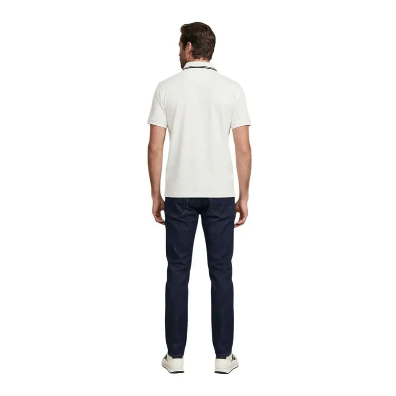 Un homme portant un Guess Polo blanc à manches courtes pour homme, mélange de coton avec bordures bleu marine, et jean foncé.