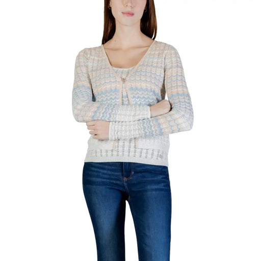 A woman wears a Guess women beige long sleeve knitted cardigan with a button v neck and textured wavy pattern