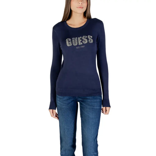 Woman wearing navy blue long-sleeved T-shirt with sparkly GUESS EST 1981 graphic