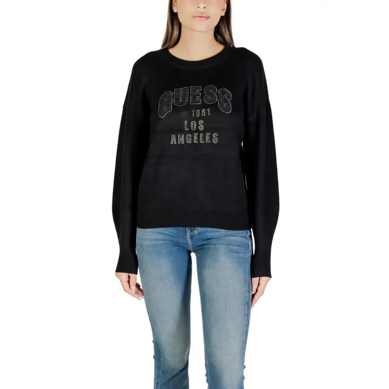 Woman wearing a black long-sleeved sweater with GUESS 1961 LOS ANGELES silver text and blue jeans