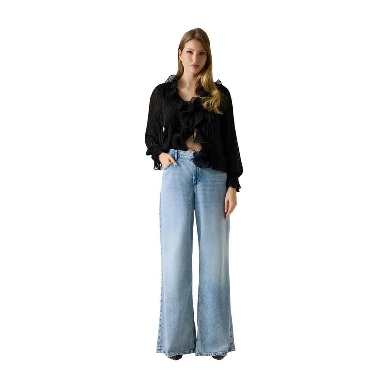 Une femme portant Guess Jean bleu ample en lyocell mélangé pour femme, porté avec un chemisier noir à volants et manches transparentes.