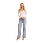 Une femme porte un guess Pull blanc à col en V pour femme, en viscose mélangée, avec manches longues crème et jean large délavé clair.