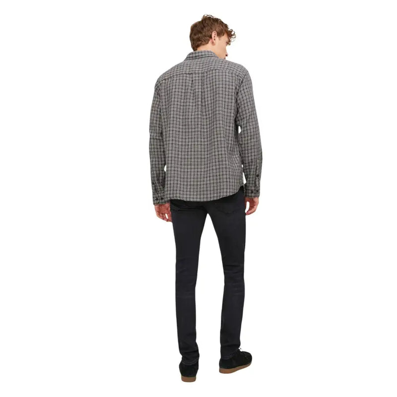 Un homme portant une chemise à carreaux noirs et blancs à manches longues et col boutonné, ainsi qu'un jean noir Jack & Jones pour homme