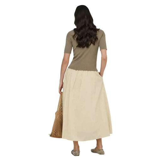 Une femme porte une jupe longue beige en coton de Jacqueline de Yong, avec une taille plissée et de discrètes poches latérales.