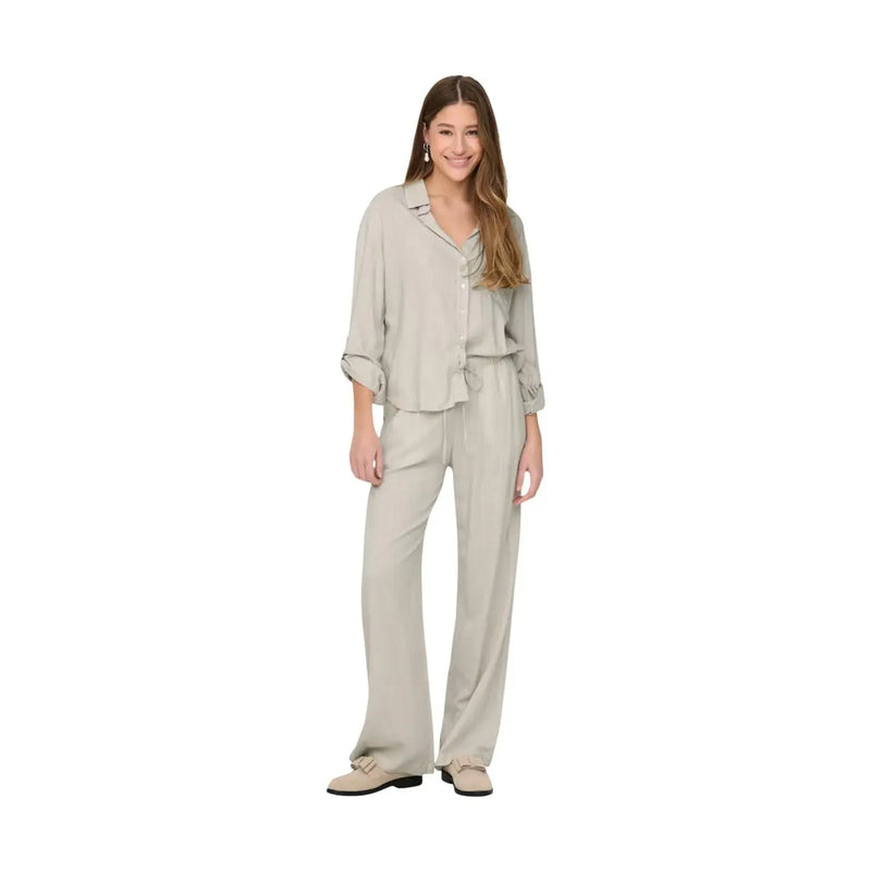 A woman wears a coordinated beige linen button-up shirt with rolled sleeves and matching wide-leg trousers