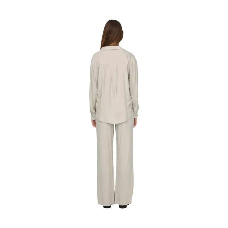 A woman wears the back of a beige Jacqueline De Yong women grey linen v neck loose shirt with subtle pleats