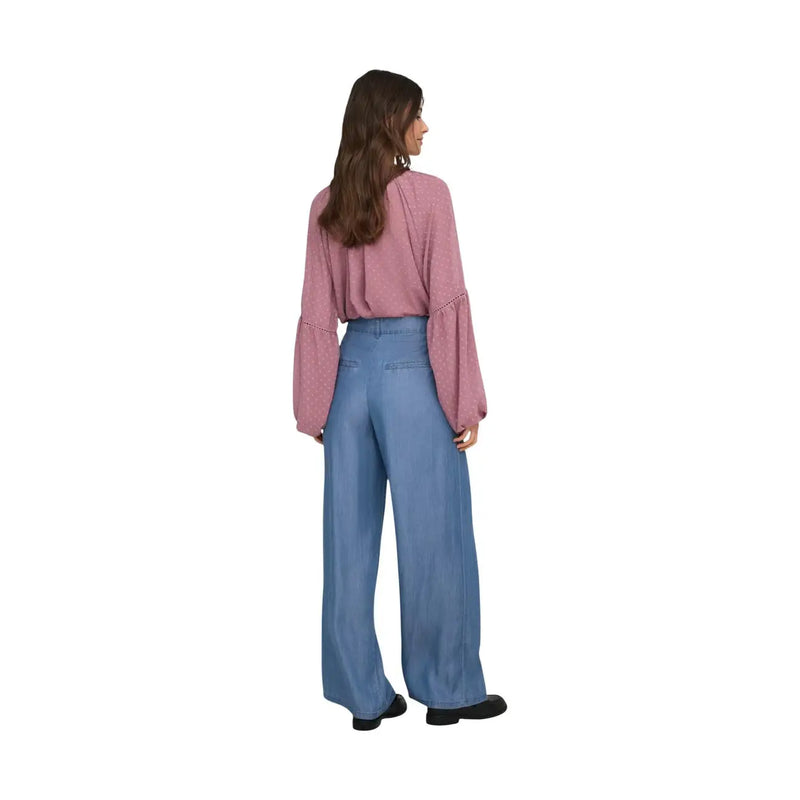 Une femme portant un pantalon large bleu en lyocell Jacqueline de Yong, associé à un chemisier rose pâle à manches évasées.