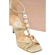 Sandales Jimmy Choo pour femme en cuir beige avec finition métallisée dorée, talon aiguille, bout ouvert et ornements de perles blanches.
