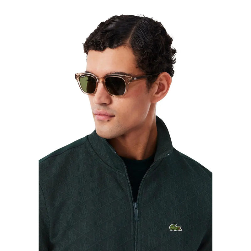Lunettes de soleil Lacoste à monture en acétate marron et verres rectangulaires vert foncé, portées avec un sweat-shirt à capuche en coton vert.