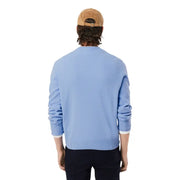 Pull Lacoste pour homme, en maille bleu clair, col rond, en laine, poignets et ourlet côtelés, assorti à un bonnet en velours côtelé beige.