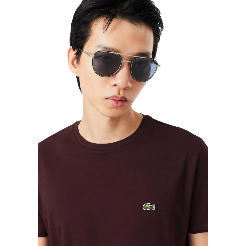 Lunettes de soleil aviateur à monture argentée et verres gris foncé, portées avec un t-shirt Lacoste homme bordeaux en coton.