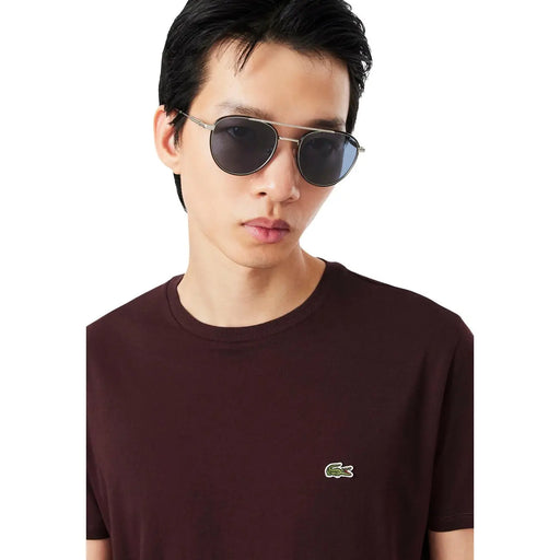 Lunettes de soleil aviateur à monture argentée et verres gris foncé, portées avec un t-shirt Lacoste homme bordeaux en coton.