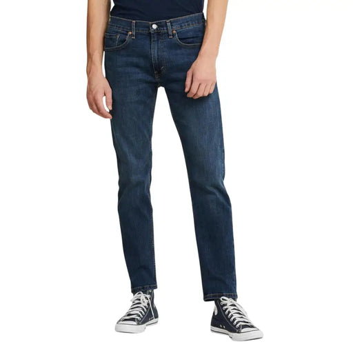 Dark blue levi’s 501 straight leg jeans with white stitching and black converse sneakers.