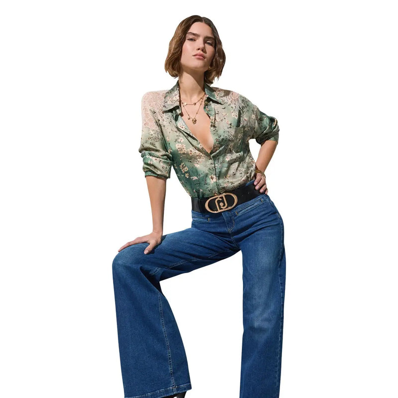Une femme porte Liu Jo Jean large en coton stretch bleu pour femme, porté avec un chemisier en soie verte à fleurs et une ceinture noire