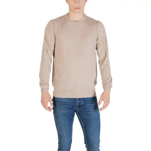 Man wearing a beige long-sleeved sweater and blue jeans suitable for casual wear