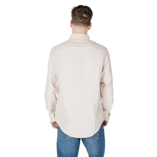 Man wearing a beige long-sleeved button-down shirt and blue jeans