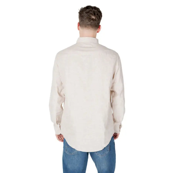 Man wearing a beige long-sleeved button-down shirt and blue jeans