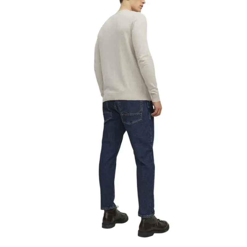 Man wearing a beige crew neck sweater and dark blue jeans displayed in the product listing