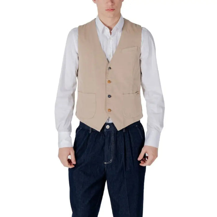 Man wearing a beige vest and blue pants styled with a navy vest and white shirt