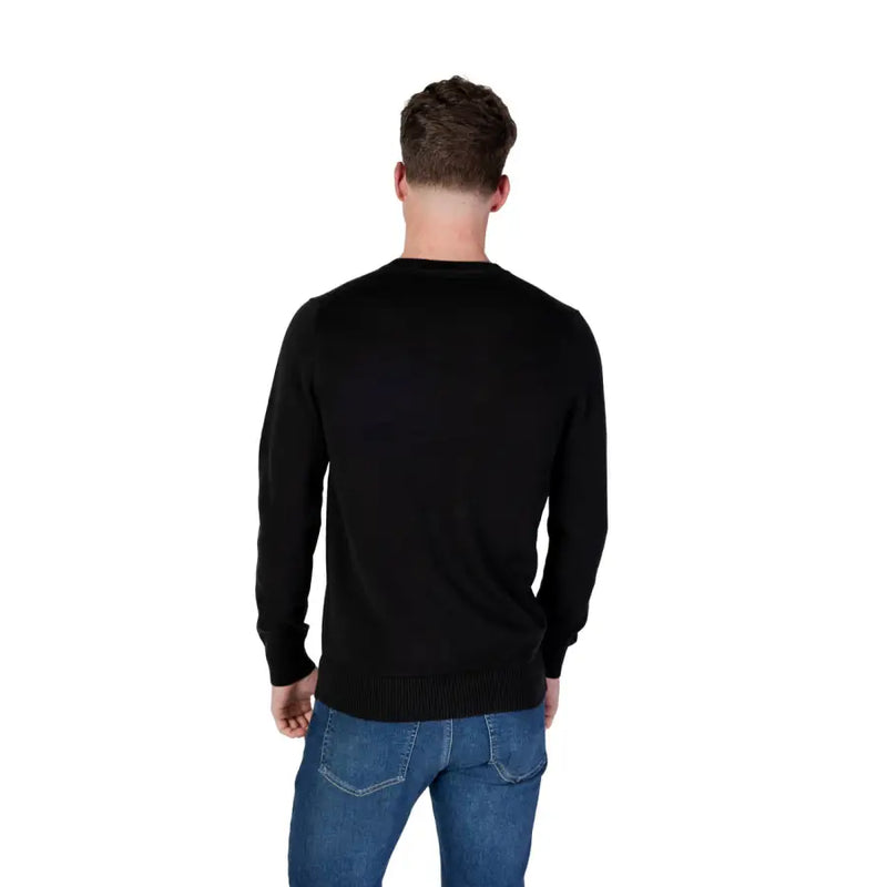 Man wearing a black long-sleeved shirt and blue jeans, showcasing Calvin Klein Black Crewneck Sweater