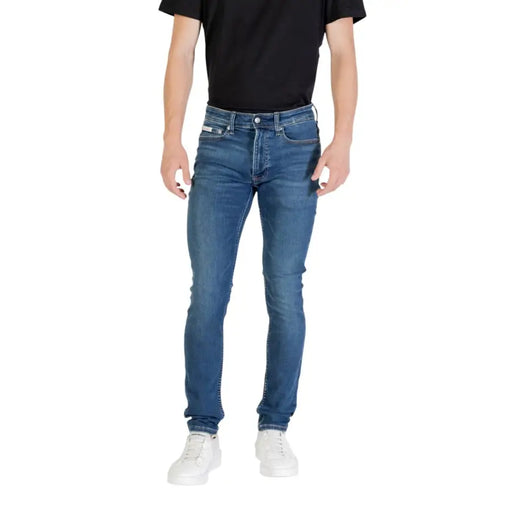 Man wearing blue denim skinny jeans and white sneakers demonstrating men’s fashion style
